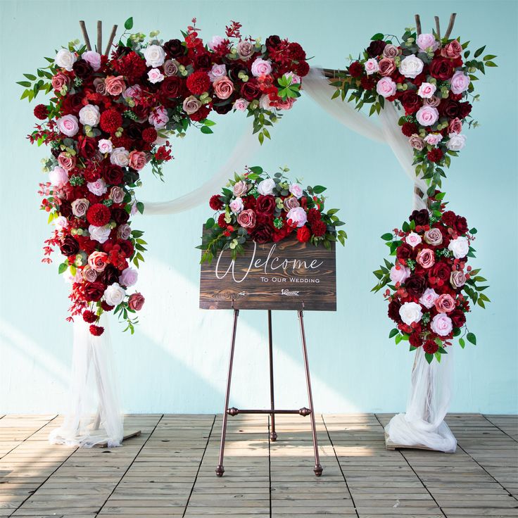 a welcome sign with flowers on it next to a wooden sign that says welcome and stands in front of a blue wall