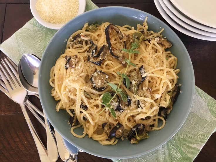 a blue bowl filled with pasta and mushrooms on top of a table next to silverware