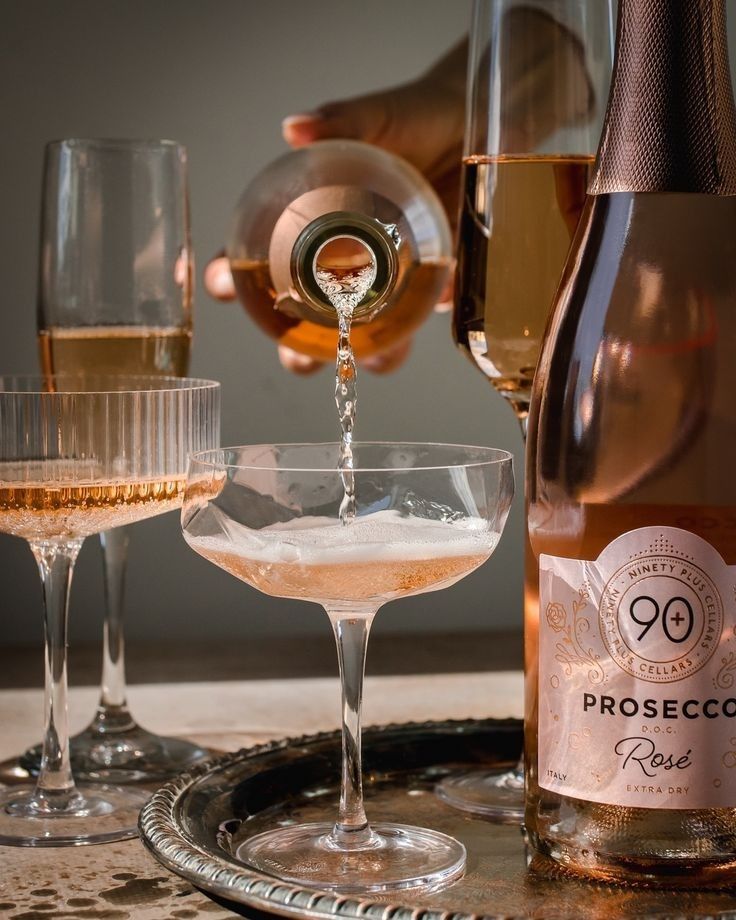 a person pours champagne into two wine glasses on a tray with another glass and bottle in the background