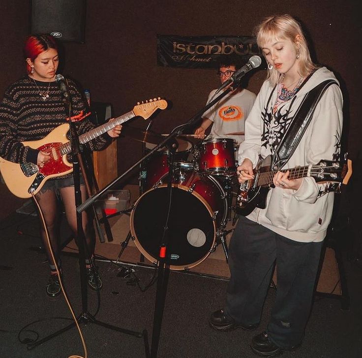 two young people are playing guitars and singing into microphones while another person stands behind them