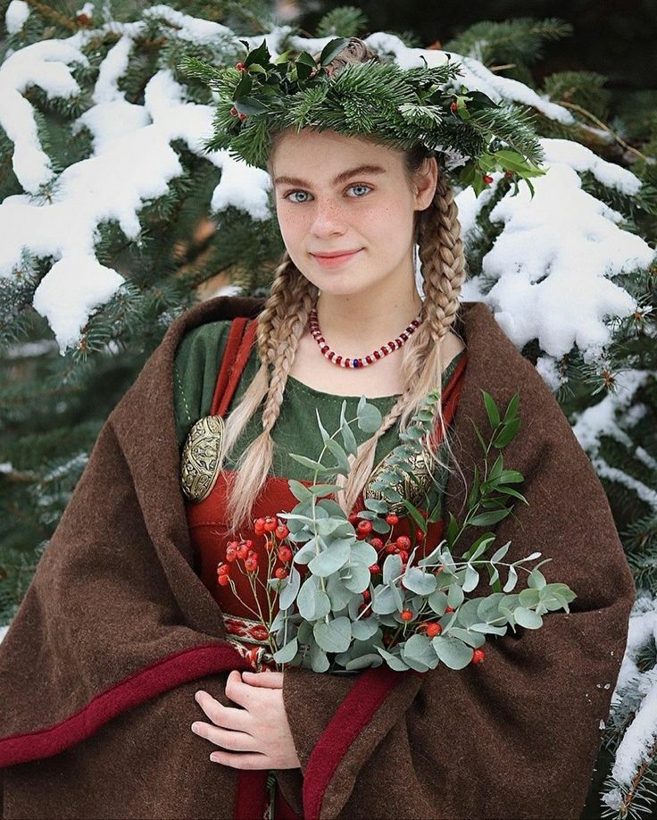 a woman wearing a brown cloak and holding a bouquet of flowers in her hands with snow on the ground behind her