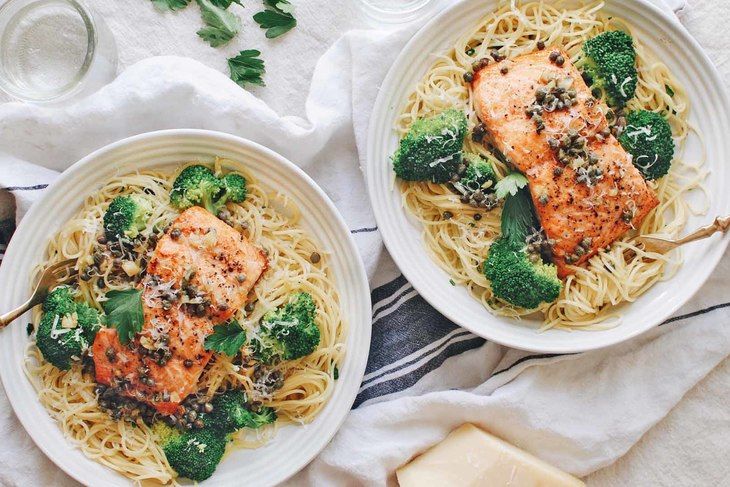 two white bowls filled with pasta and broccoli on top of a table next to cheese