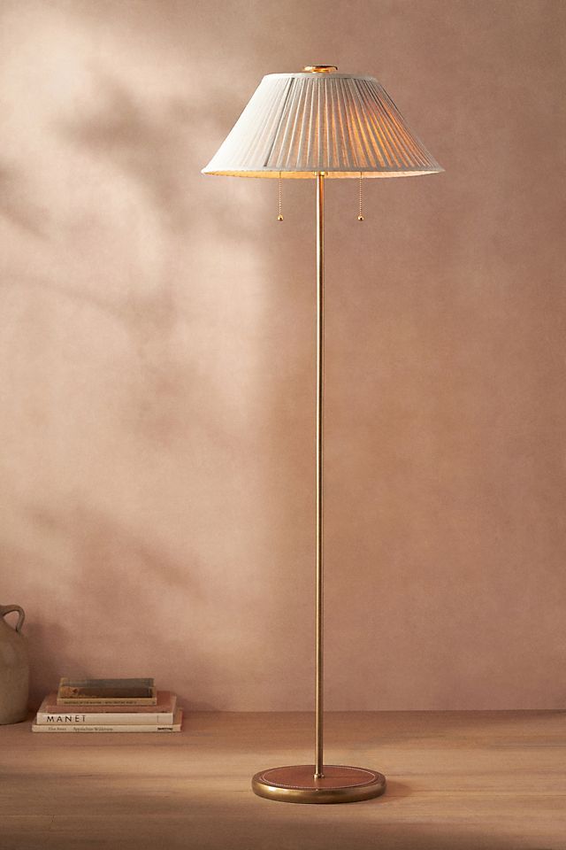 a floor lamp with a white shade on it and a book shelf in the corner