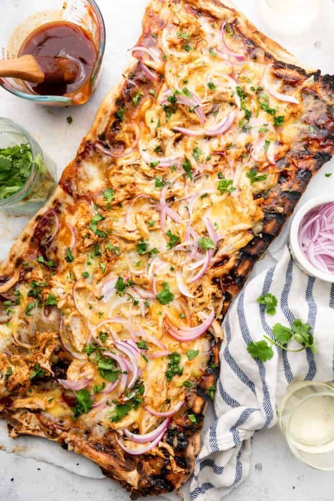 an overhead view of a pizza with onions and herbs on it, next to some condiments