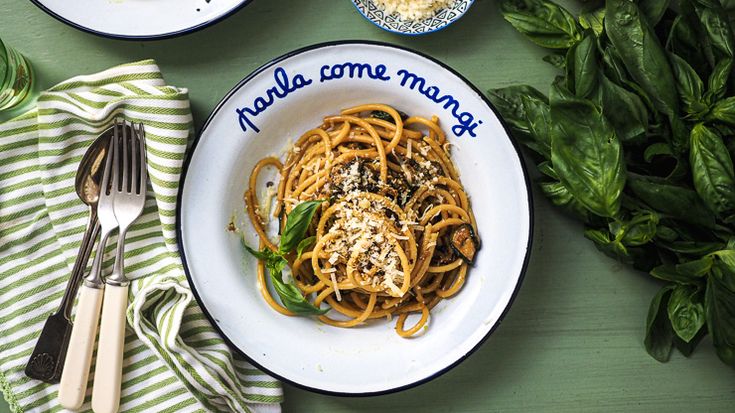 two plates of spaghetti with basil, parmesan cheese and bread on the side