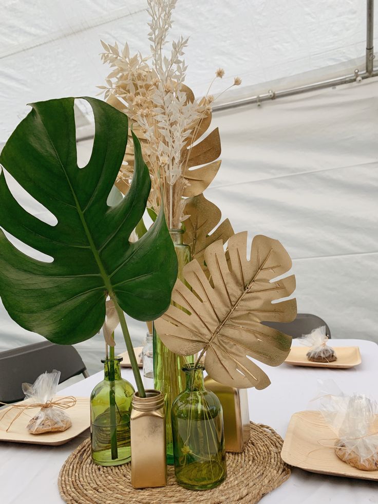 a table topped with green vases filled with plants and greenery next to plates