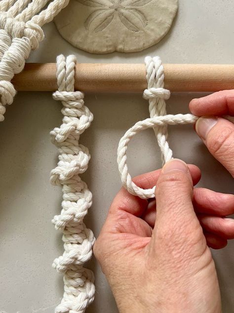 two hands are working on a piece of white yarn that is attached to a wooden stick