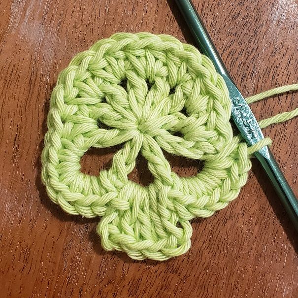 a crocheted skull is sitting on a wooden table next to a knitting needle