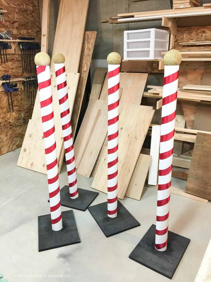 three red and white striped poles are standing on black bases in front of wood boards