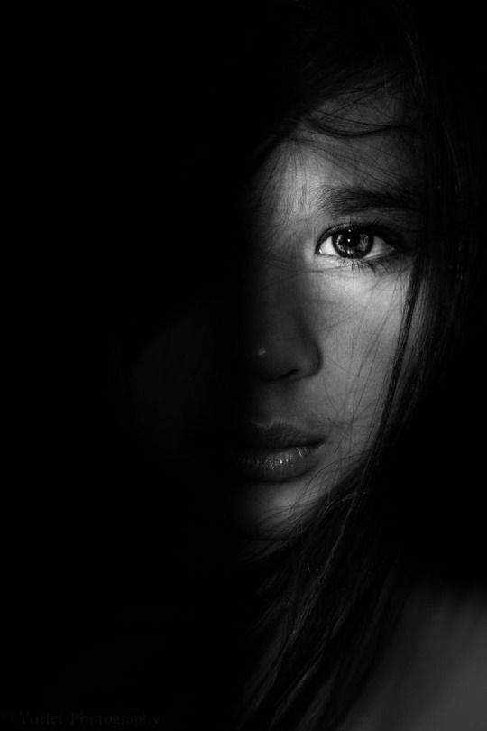 a black and white photo of a woman's face with long hair in the dark