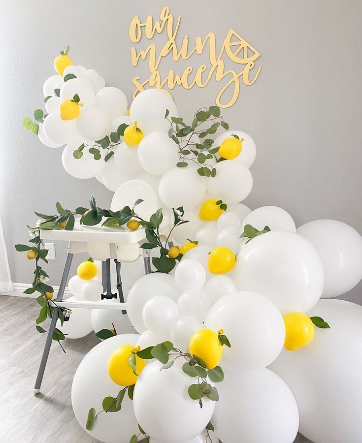 white balloons with yellow flowers and greenery are arranged in front of a cake table