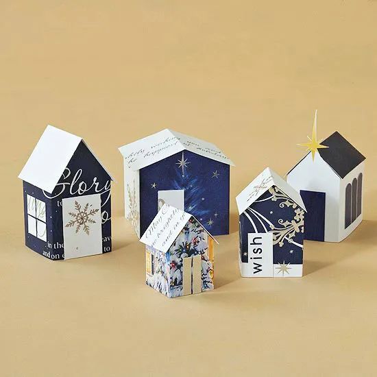 three small houses made out of paper on top of a brown surface with stars and snowflakes