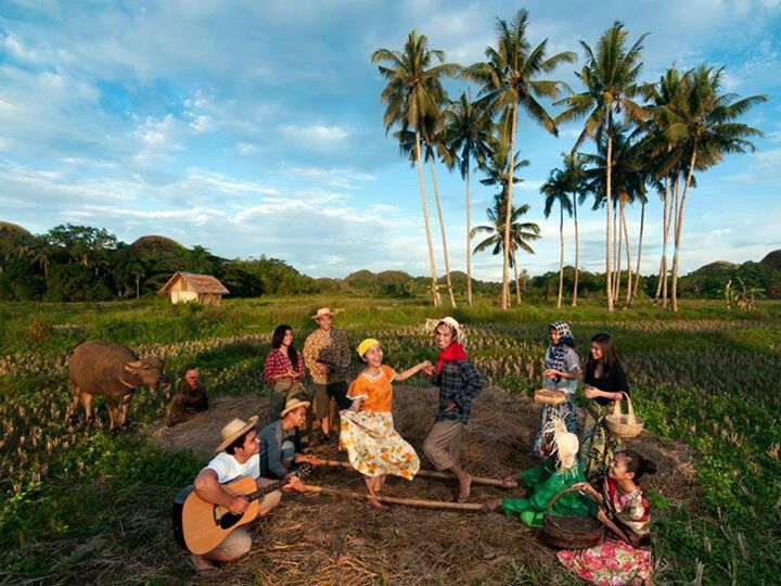 a group of people sitting on top of a lush green field next to palm trees