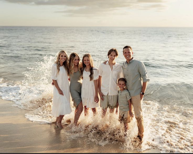 a family standing in the surf at the beach with their arms around each other as they pose for a photo