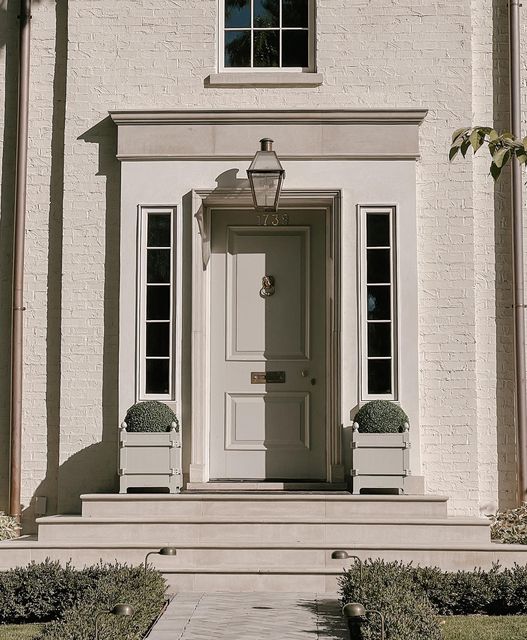 a white house with two chairs and a light on the front door is pictured in this image