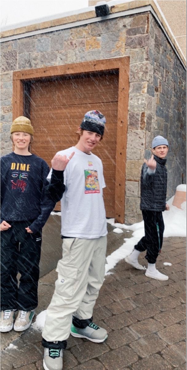 three young boys standing in front of a garage door with snow falling on the ground