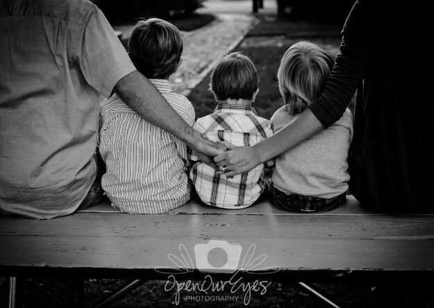 black and white photograph of family sitting on park bench with their arms around each other