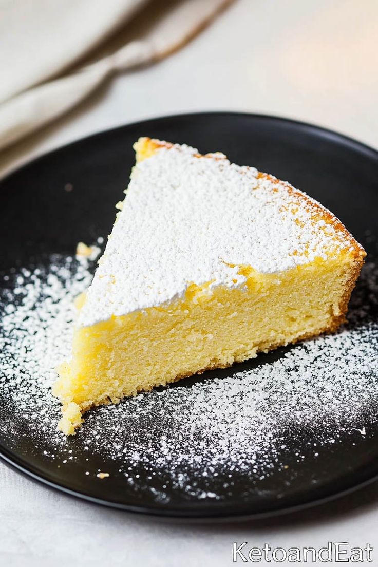 a piece of cake on a black plate with powdered sugar around it and a fork in the background