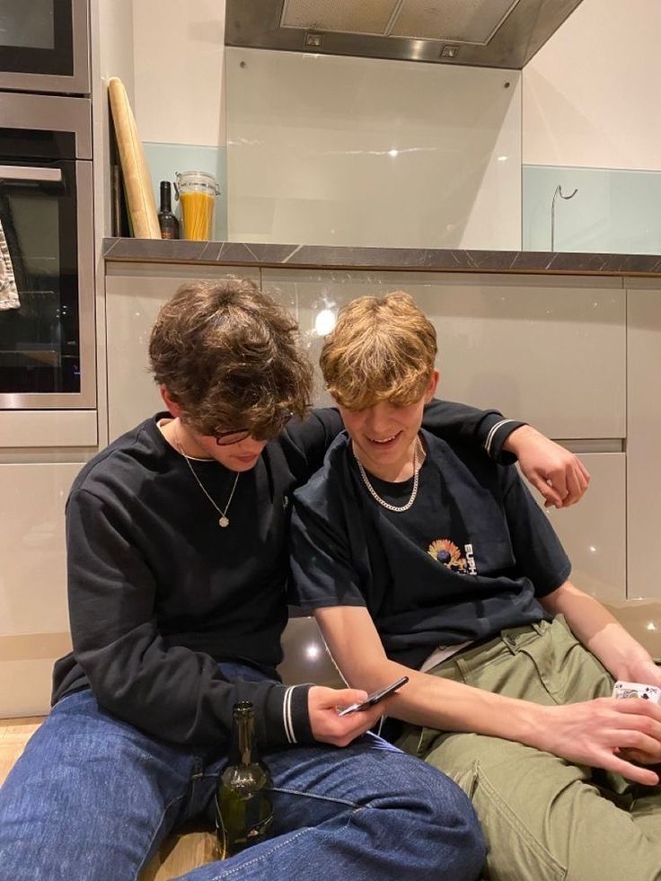 two boys sitting on the floor looking at their cell phones