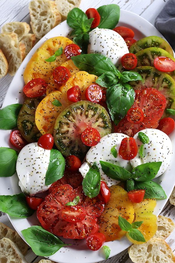 a white plate topped with sliced tomatoes and mozzarella cheese covered in basil leaves