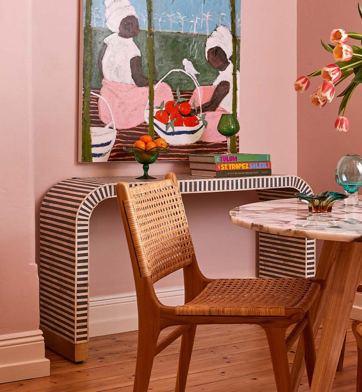 a dining table with two chairs and a painting on the wall behind it in a pink room