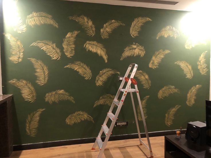 a ladder is in front of a green wall with gold palm leaves on it,