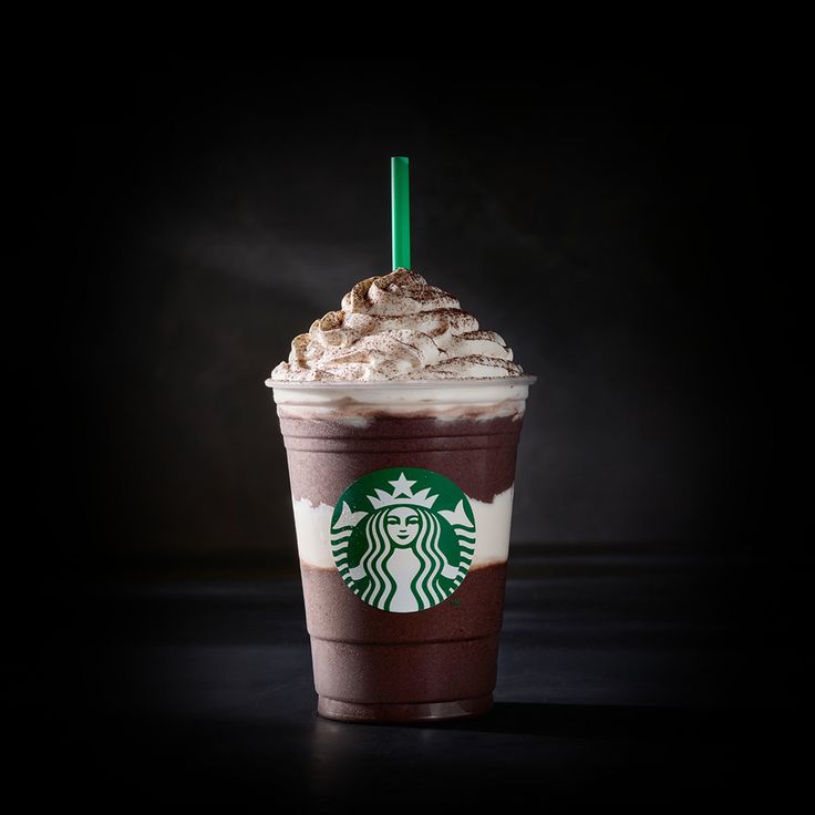 a cup of coffee with whipped cream and a green straw in it on a black background