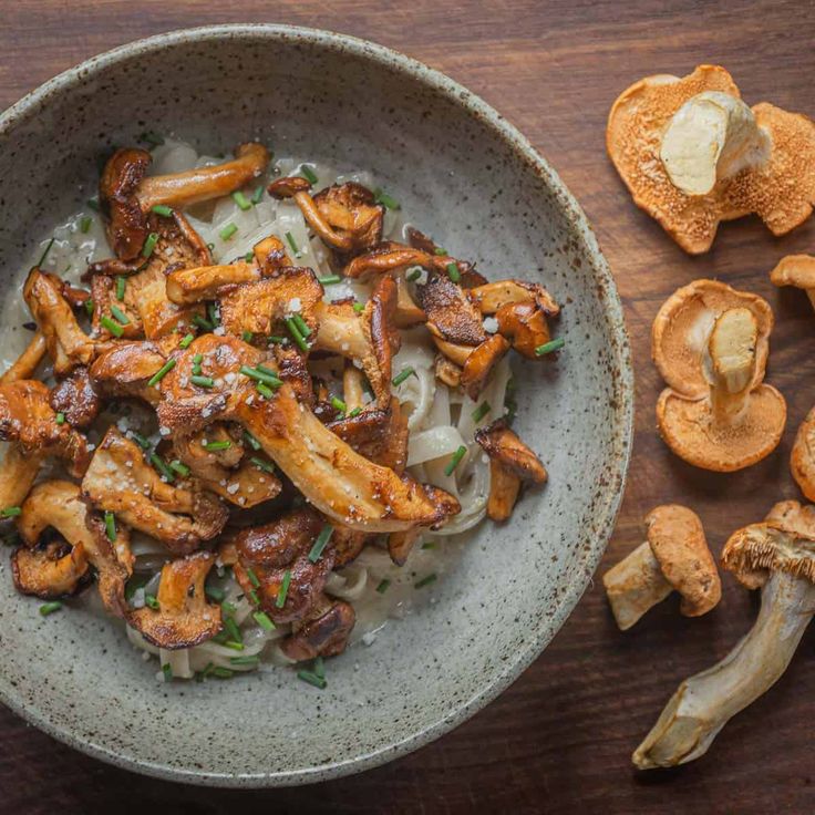 a bowl filled with noodles and mushrooms on top of a wooden table next to sliced mushrooms