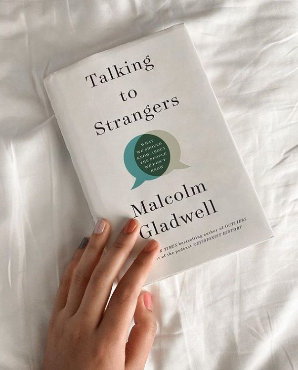 a person's hand resting on top of a book that reads talking to strangers