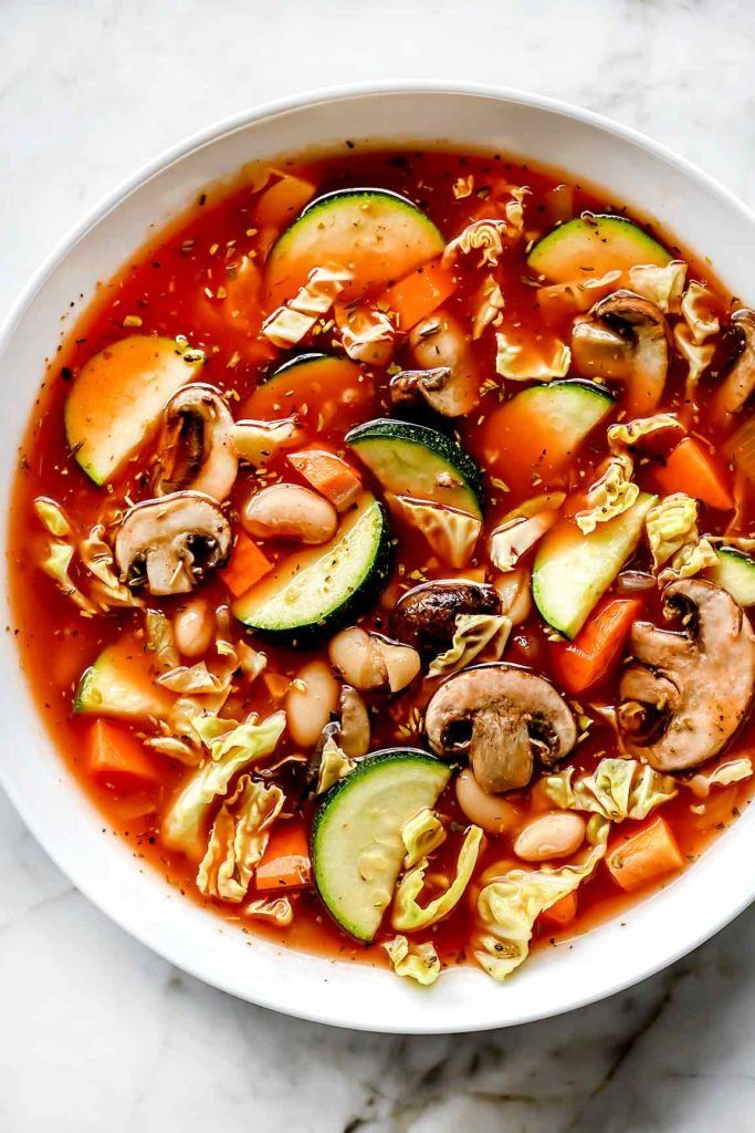 a white bowl filled with vegetable soup on top of a marble counter next to a spoon