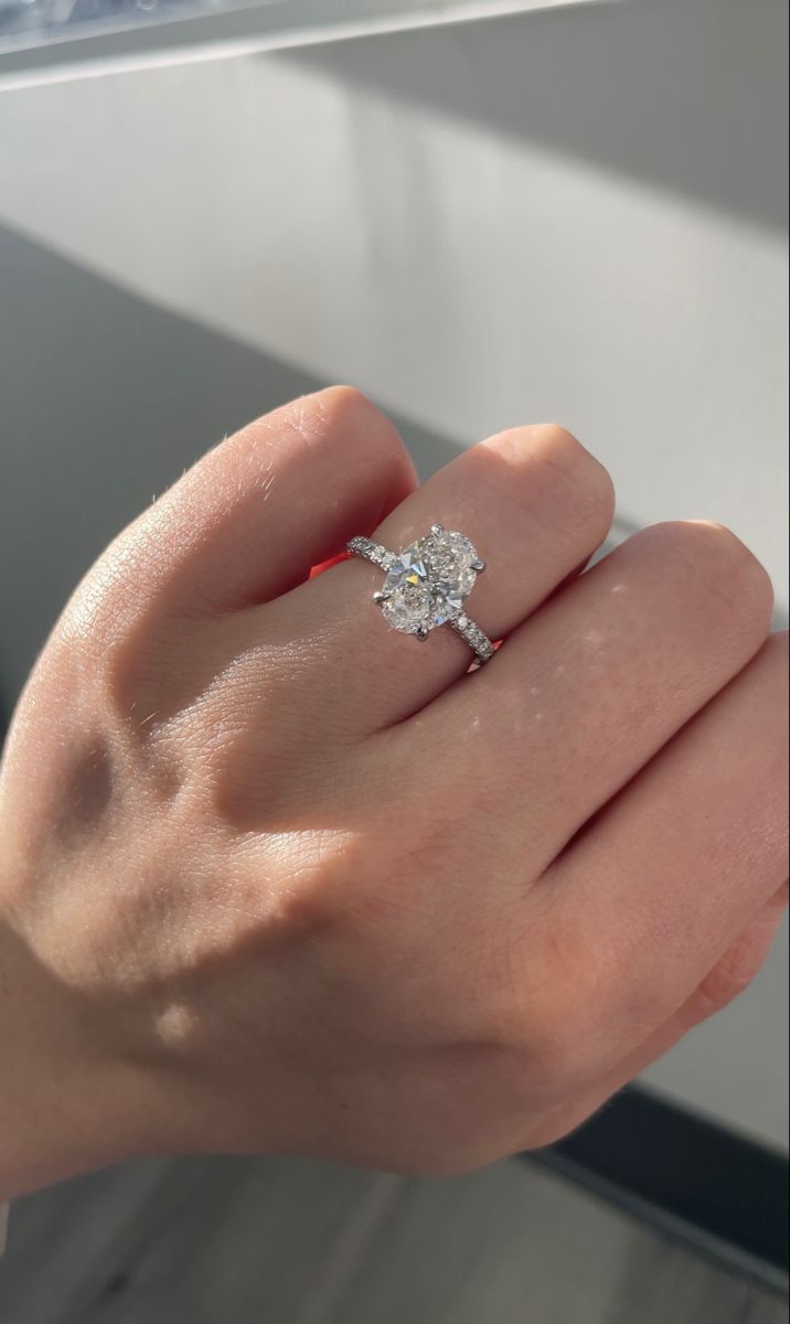 a woman's hand with a diamond ring on top of her finger, in front of a window