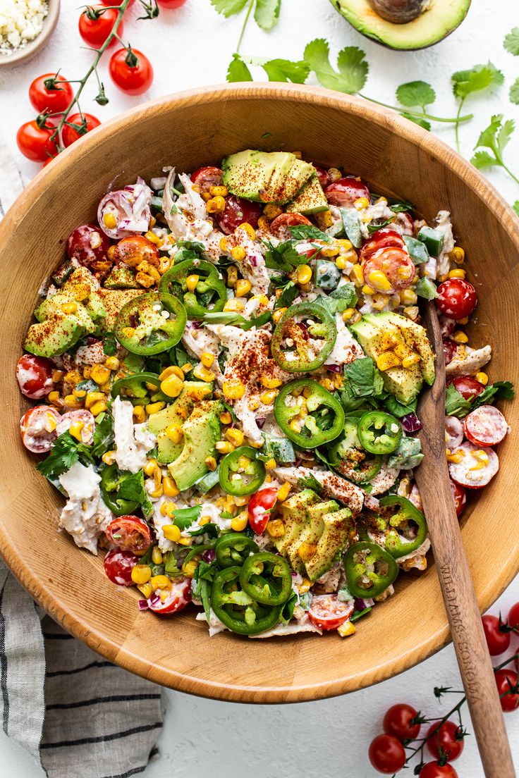 a wooden bowl filled with mixed vegetables and topped with avocado, tomatoes, corn, cucumbers, and cilantro