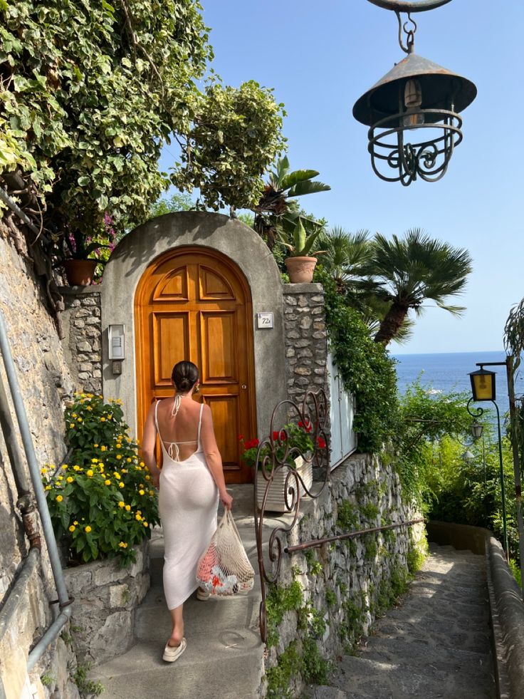 a woman is walking up the stairs to a door with flowers and potted plants