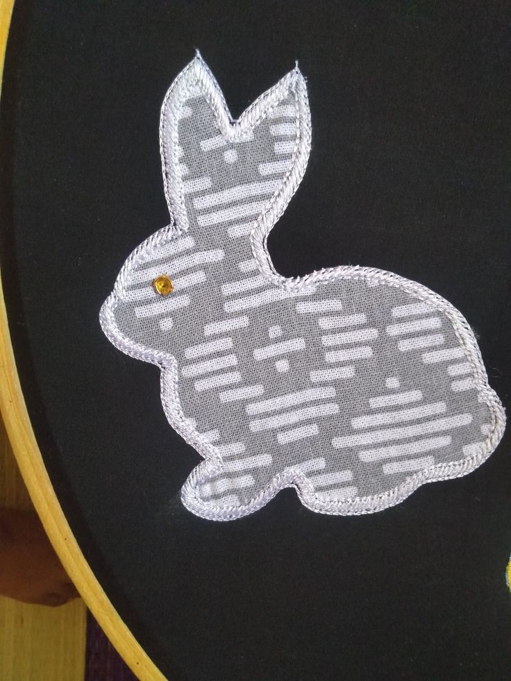 a close up of an embroidered bunny on a black background with white lines and yellow dots