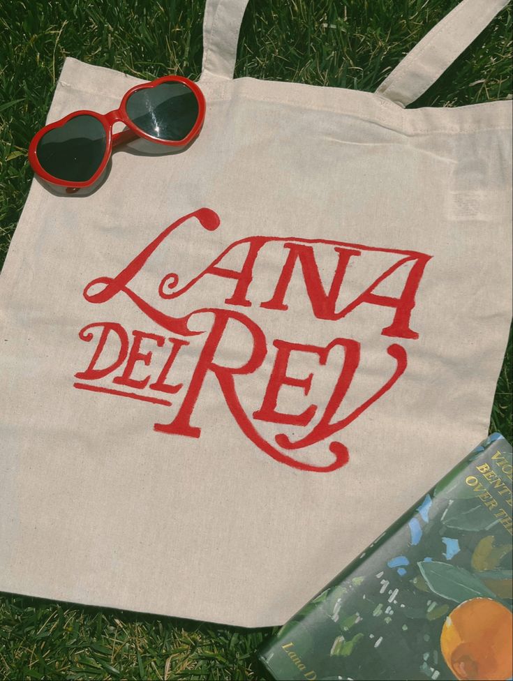 a tote bag sitting on the grass next to sunglasses