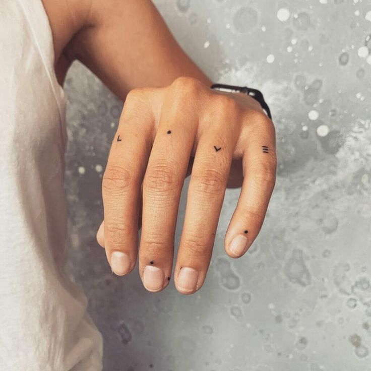 a woman's left hand with two small dots on the middle finger and an arrow tattoo