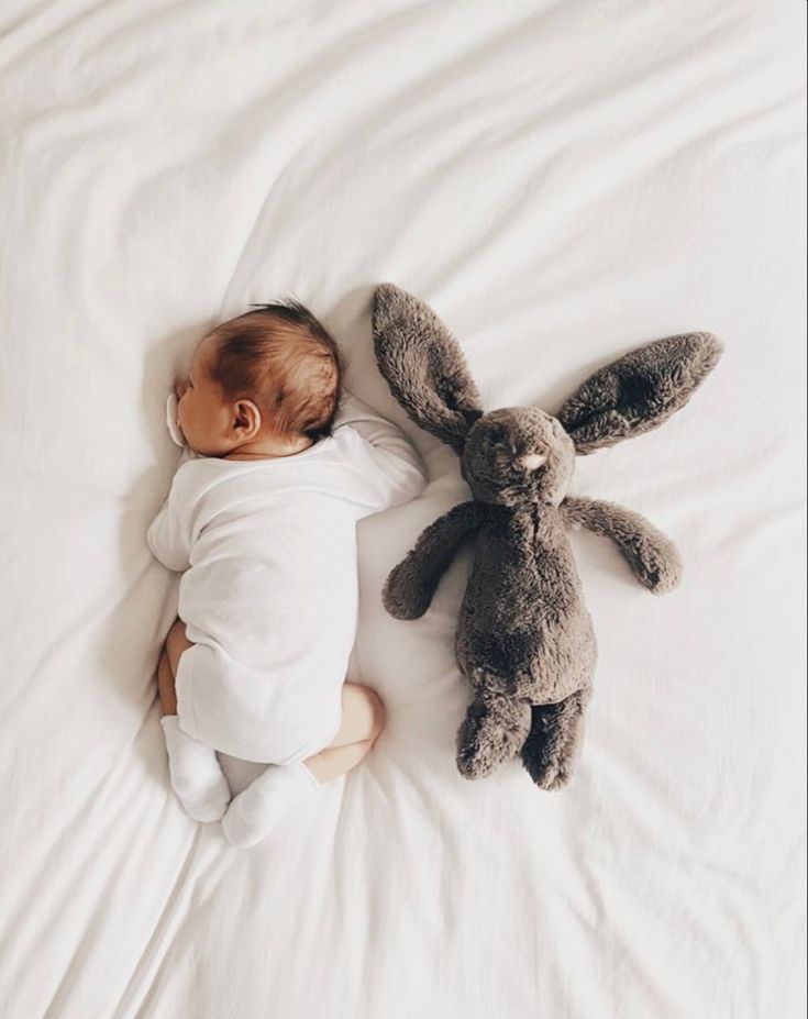 a baby sleeping next to two stuffed animals on top of a white sheet covered bed