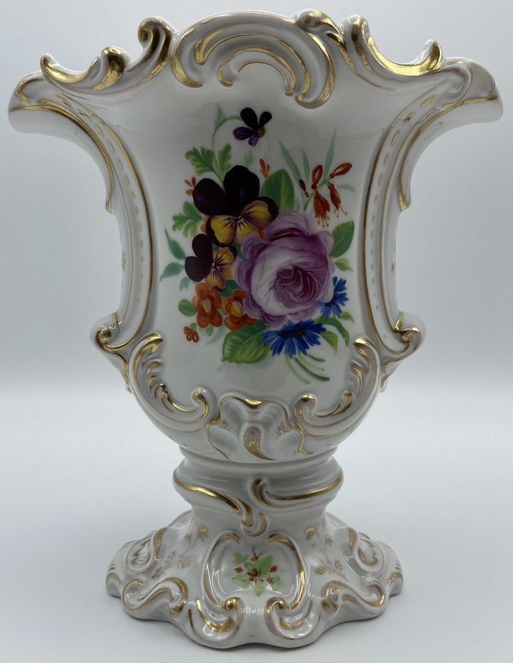 an ornate white vase with gold trimming and flowers painted on the side, sitting on a pedestal