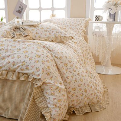 a bed with white and yellow flowers on it in front of two windows next to a table