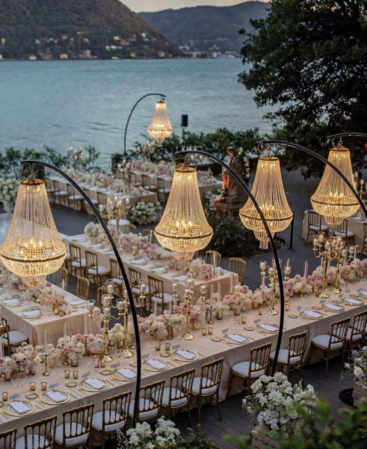 an outdoor dining area with chandeliers and tables set up for dinner by the water