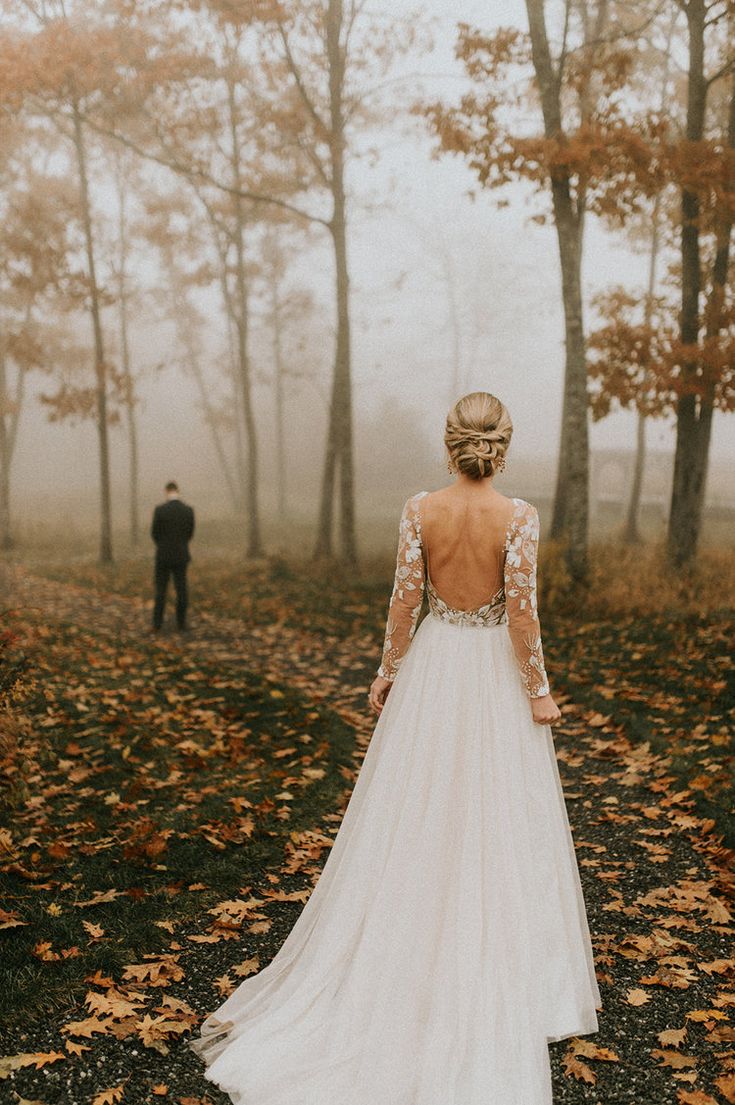 the back of a bride's dress as she walks through an autumn foggy forest