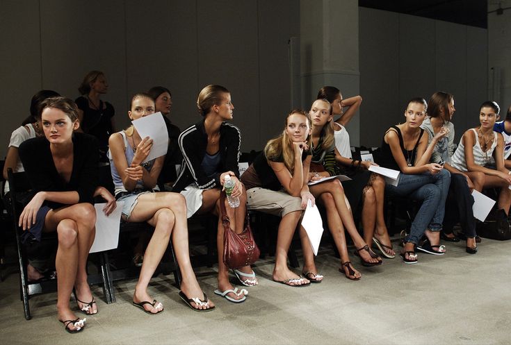 a group of women sitting next to each other in front of a crowd at a fashion show