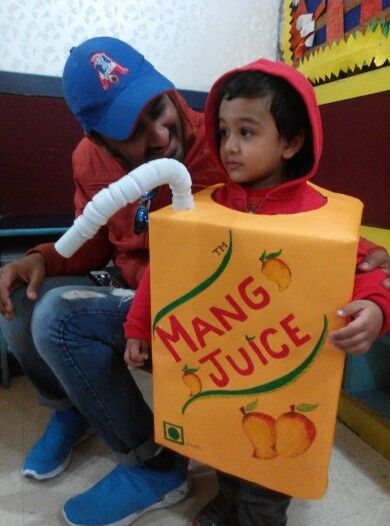 a young boy is holding a sign that says mango juice with an adult in the background