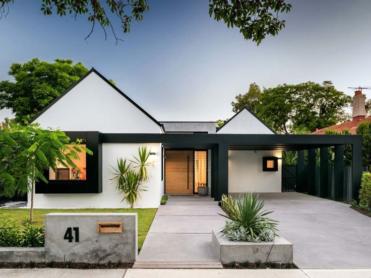 a modern house with black and white accents in the front yard, surrounded by greenery