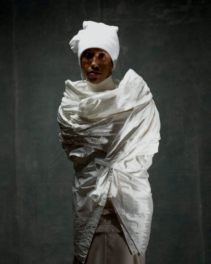 a woman with a white hat and scarf wrapped around her head, standing in front of a dark background