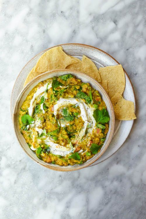 a bowl filled with guacamole and tortilla chips on top of a marble table