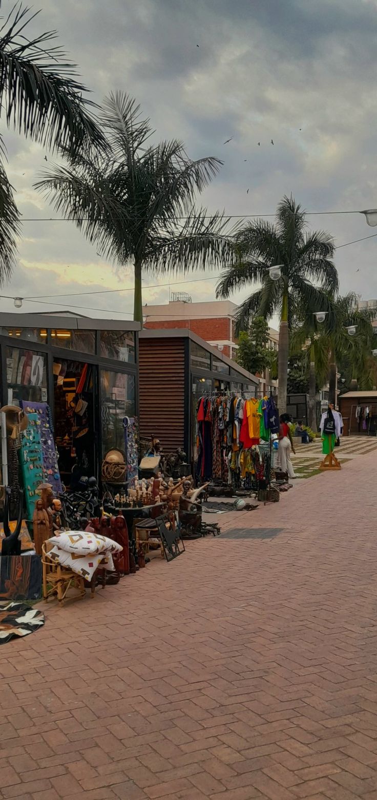 people are walking down the street near some shops and palm trees in front of them