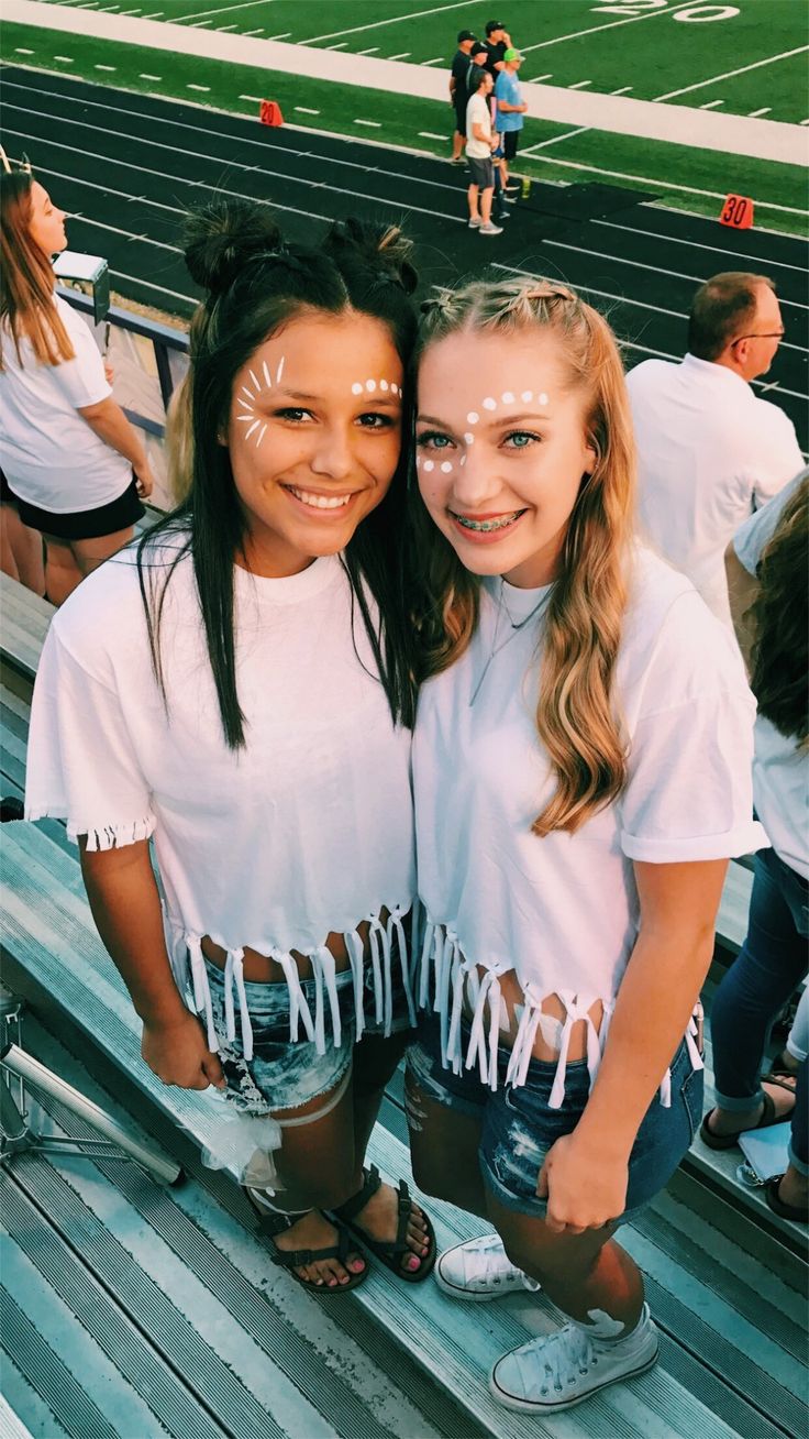 two girls with face paint on their faces posing for the camera at a football game