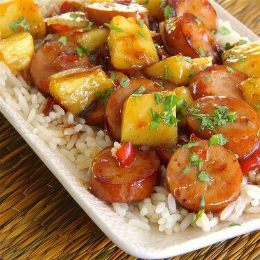 a white plate topped with pineapple and sausage covered in gravy next to rice