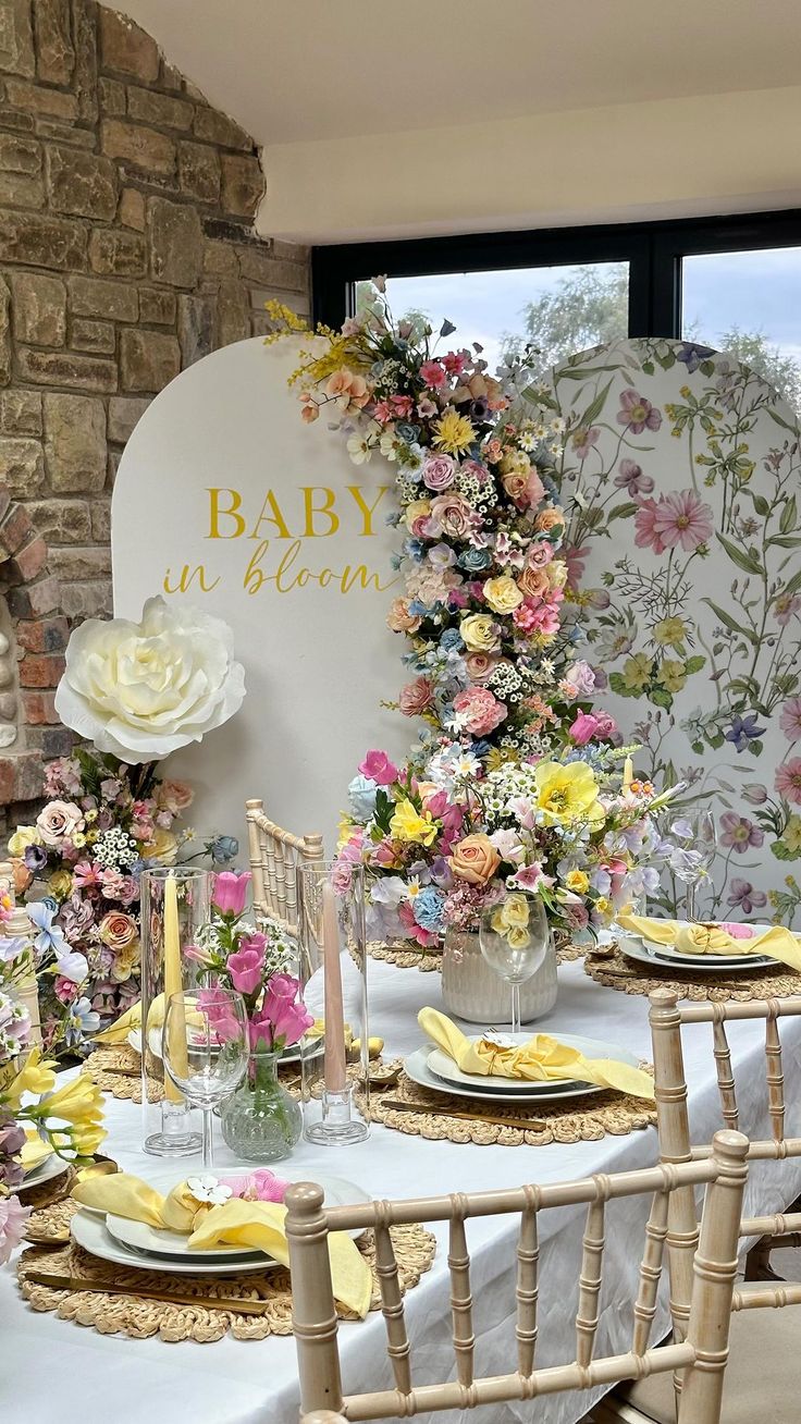 a table set up for a baby shower with flowers on the wall and candles in vases